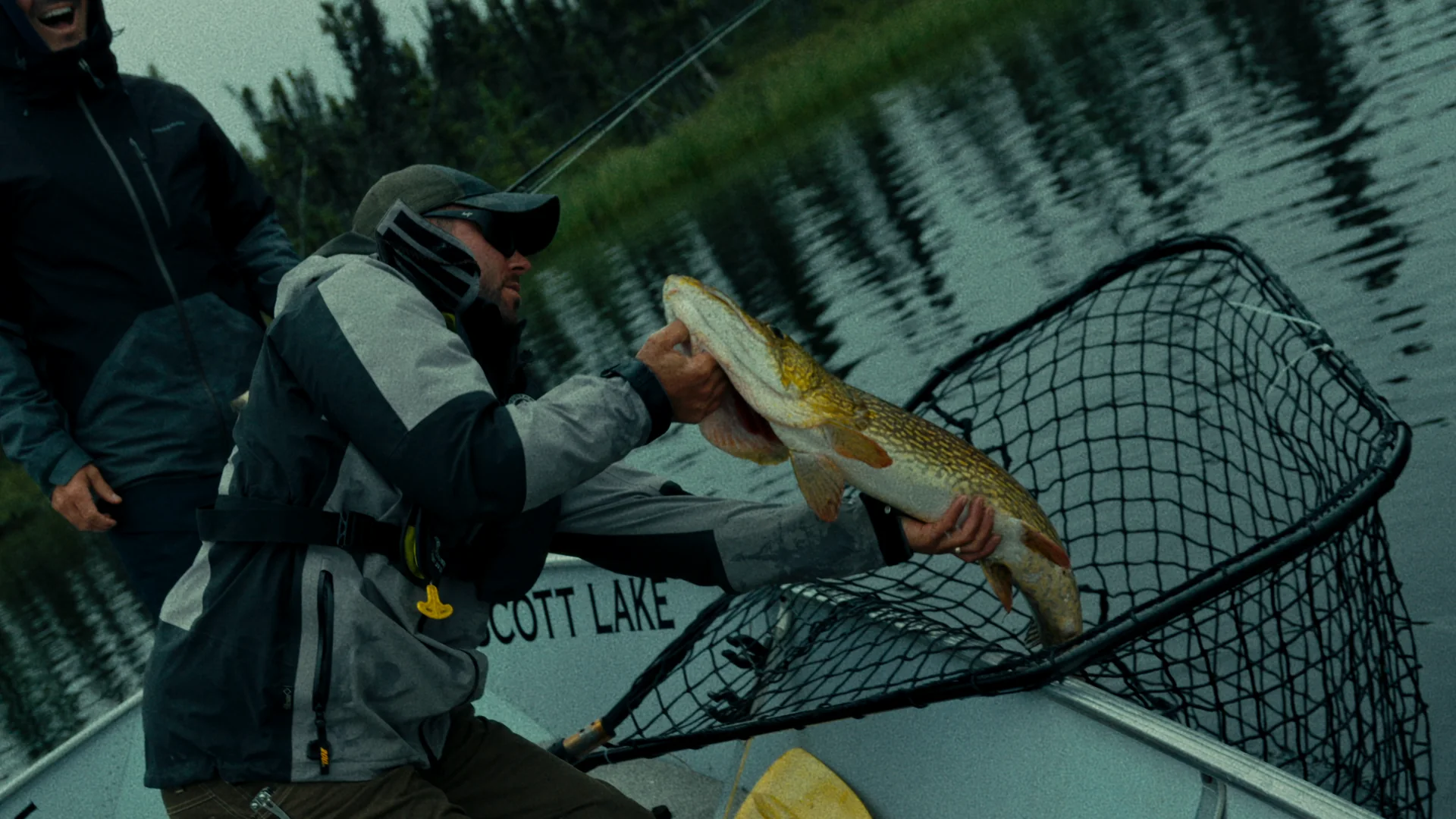 A guide lifting a pike in a landing net beside a Scott Lake boat
