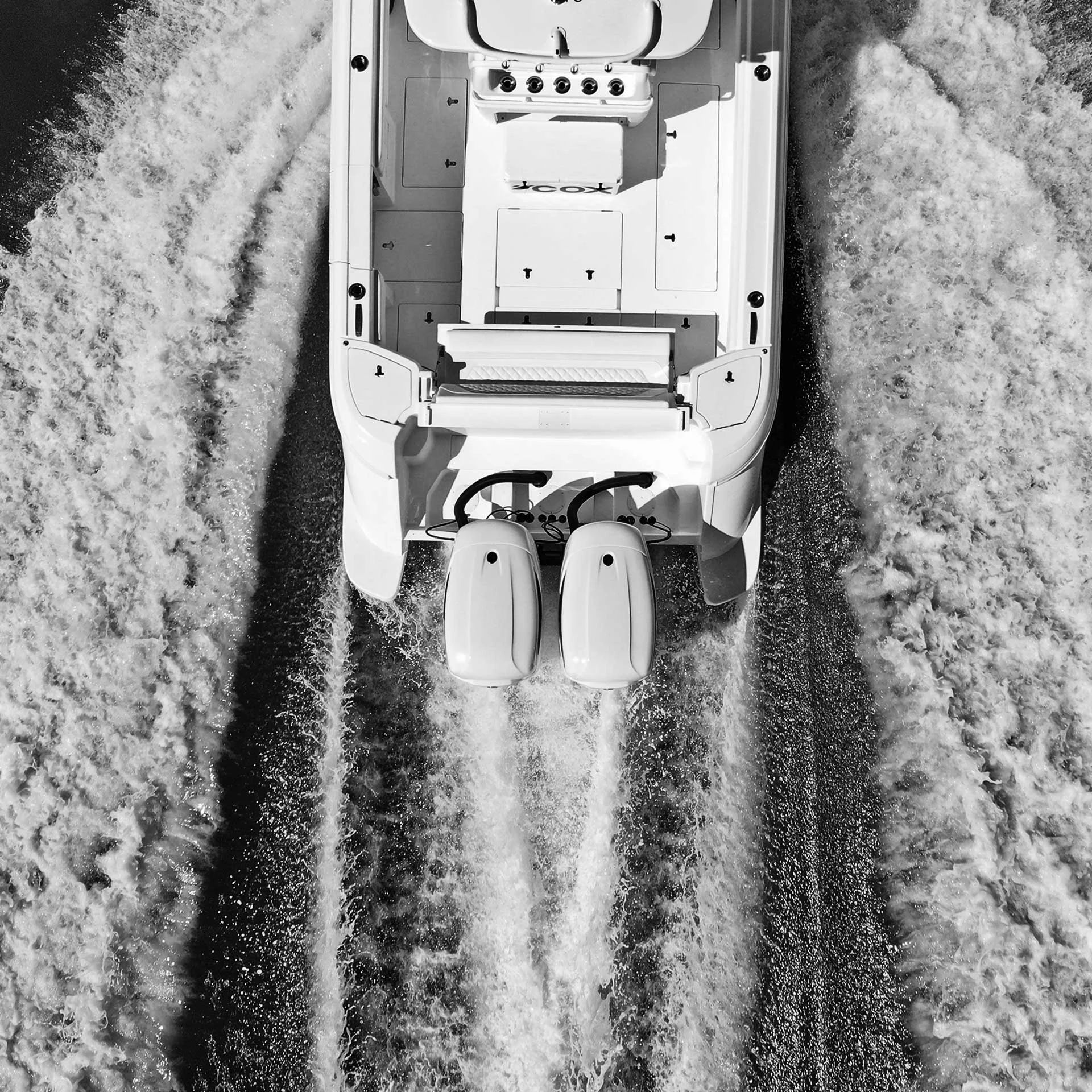 Black-and-white aerial photograph of a boat and its Cox outboards leaving a wake