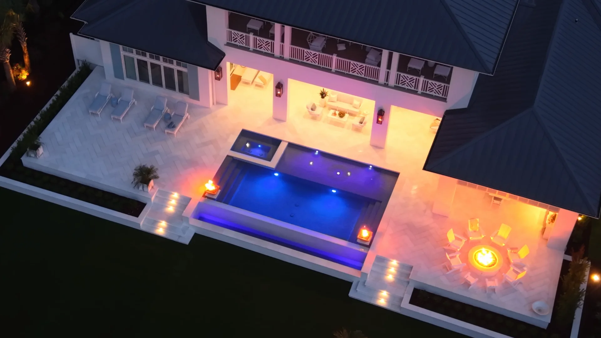 The same aerial view at dusk, with the pool, fire bowls, and fire pit lit