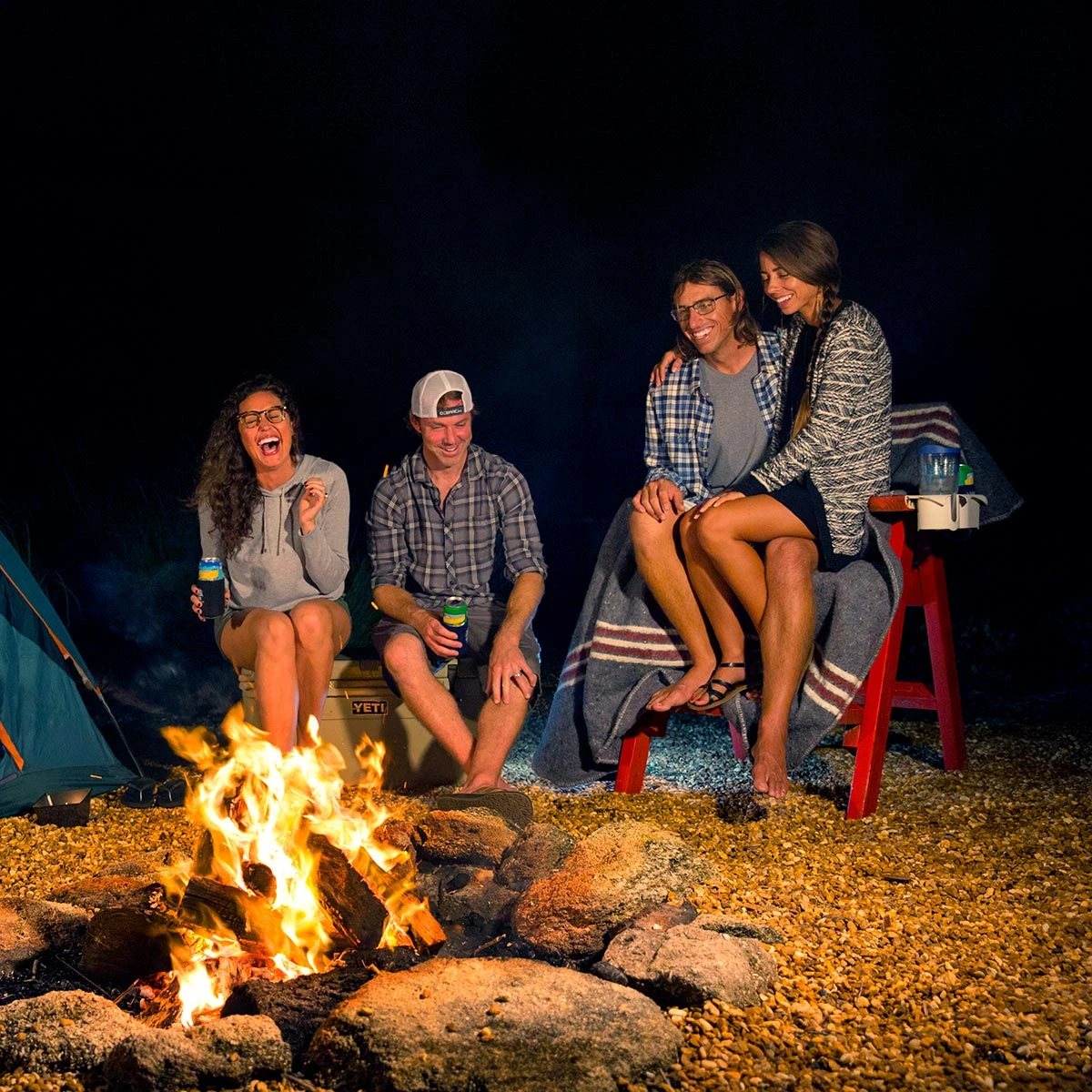 Four people wearing Costa optical glasses around a campfire at night